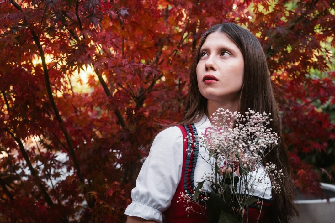 Woman in traditional dress holding flowers near red leaves