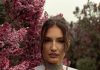 The Everyday Edit: Wardrobe Staples That Work in Every Season Woman in green top surrounded by beautiful purple lilac blossoms.